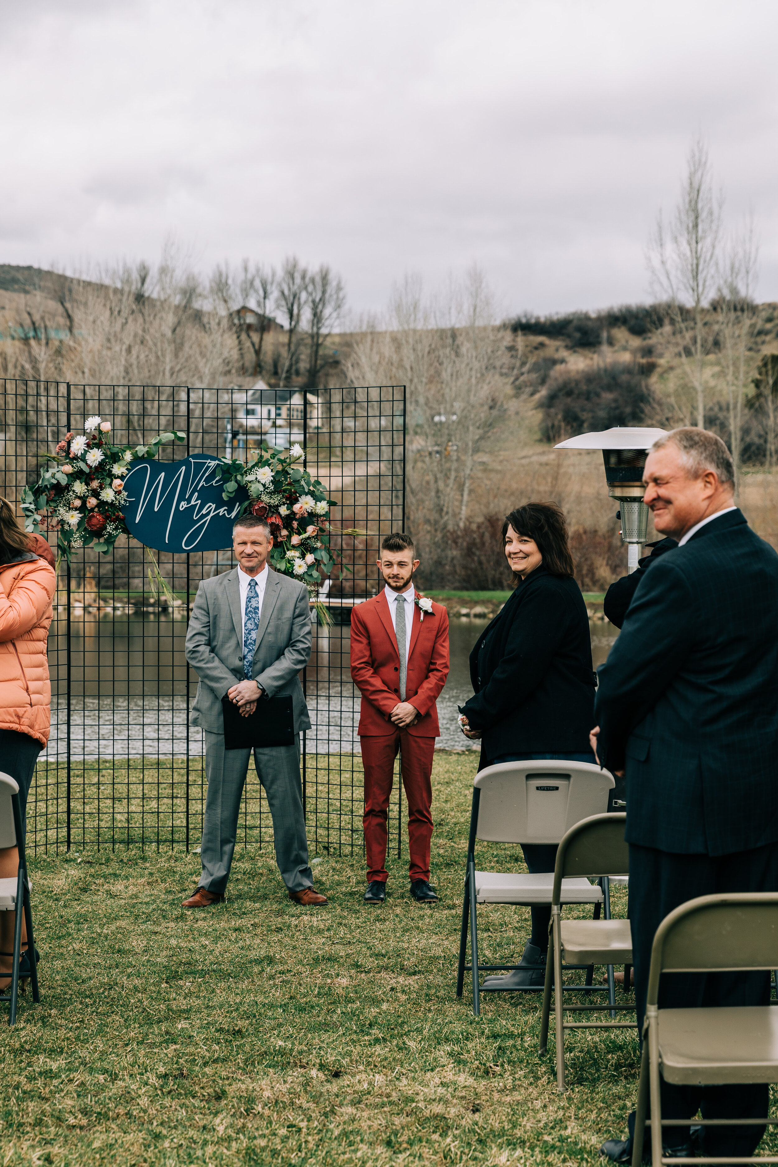  An excited groom standing at the end of the isle in a unique burgundy wedding suit in a rustic outdoor wedding session. Bella Alder Photography professional Utah photographer  unique groom wedding suit inspiration ideas and goals groom aesthetic sto