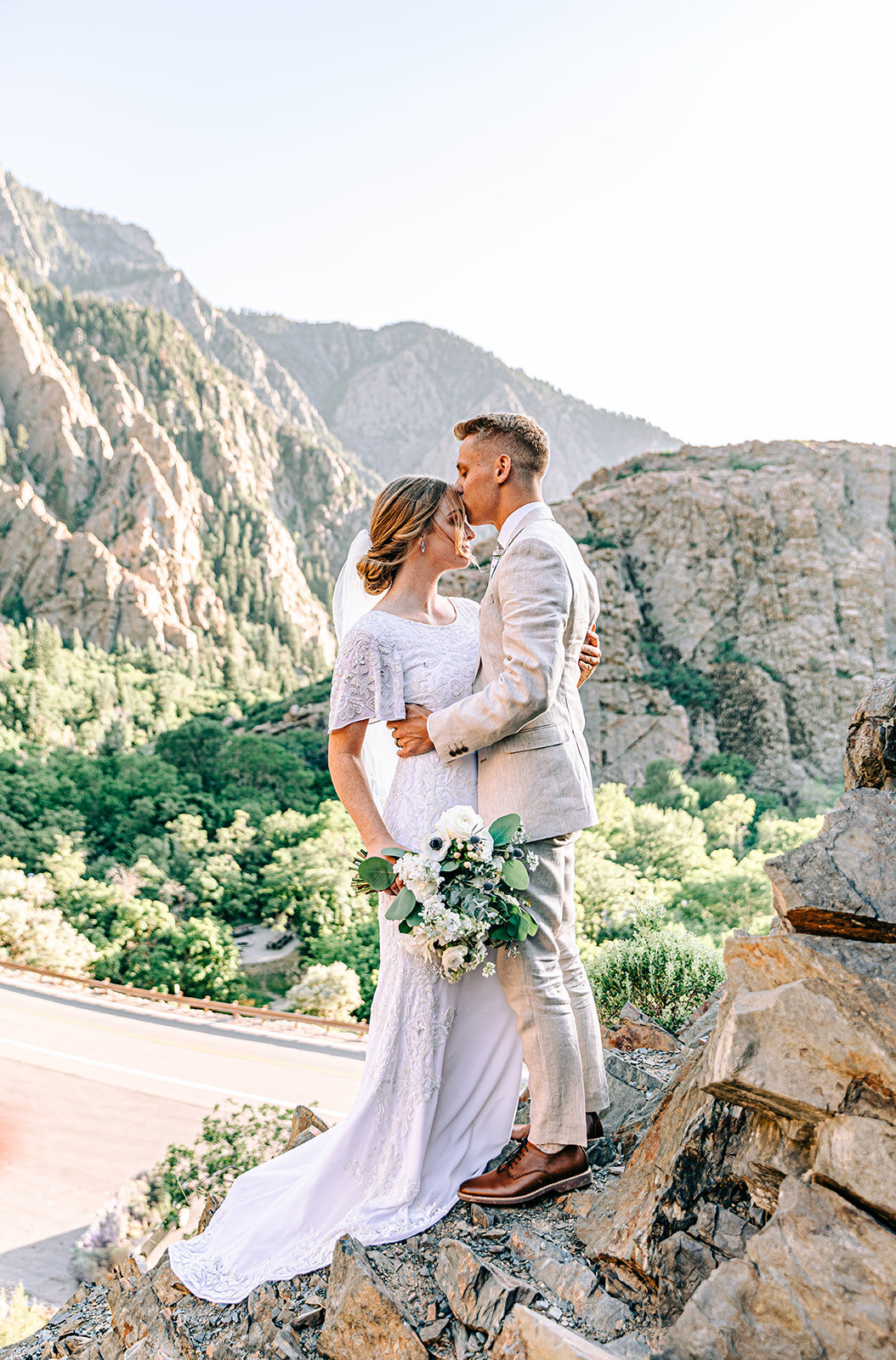  A soft kiss on the forehead of a glowing bride in a bright and airy Cottonwood Canyon in a wedding styled photo shoot. Wedding session location inspiration for modern Utah brides wedding inspiration professional Utah photographer summer wedding sess