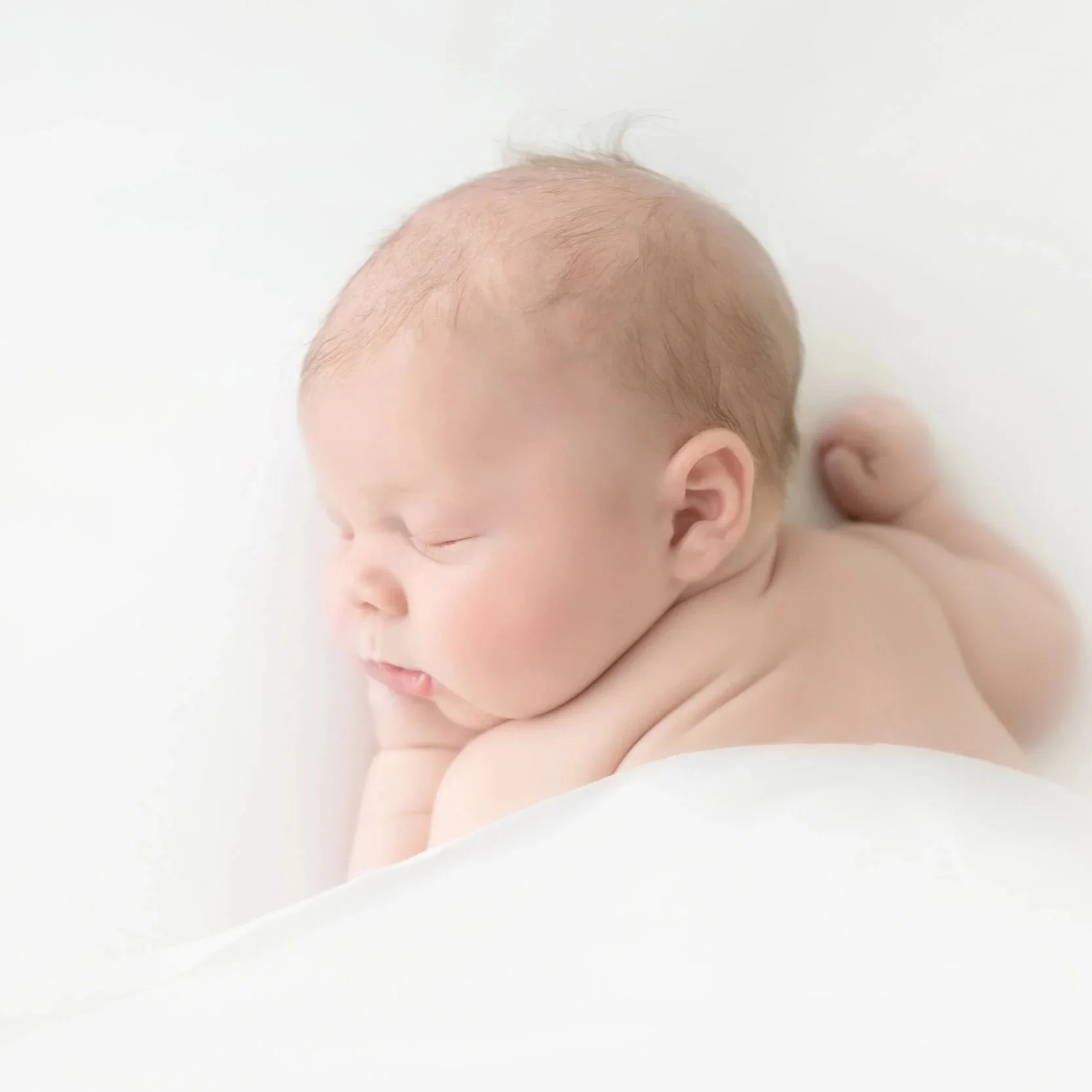 Close-up of a sleeping newborn baby with closed eyes, curled up, and minimal hair, against a white background.