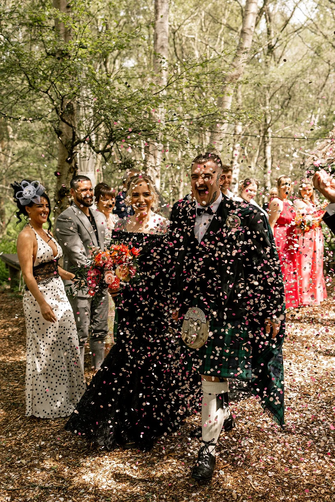 couple walk through the column of wedding guests s they throw colourful confetti over the couple