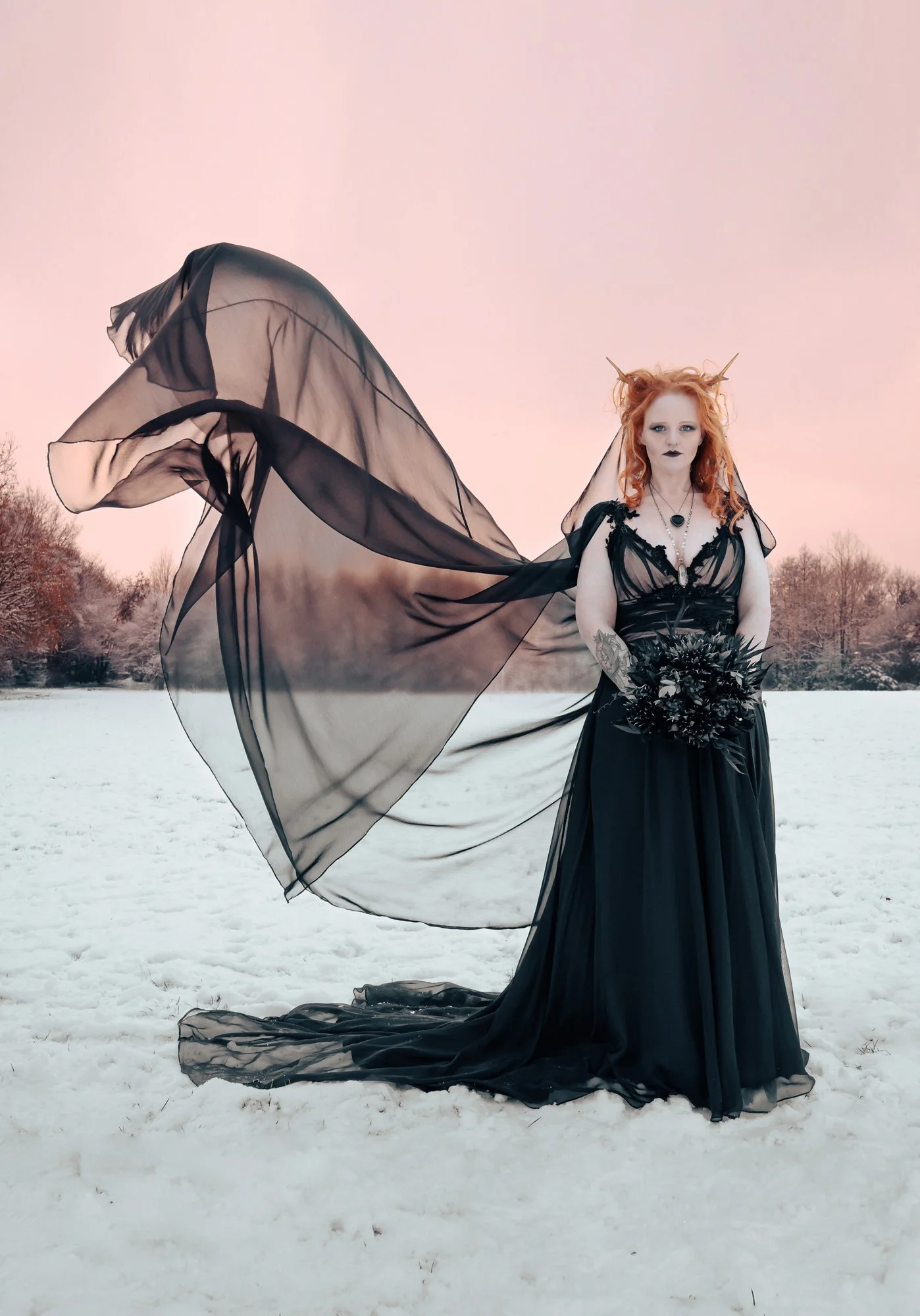 A woman dressed in a black gown outdoors on snow, holding a bouquet of dark flowers, with a flowing black cape, orange hair, and horns on her head.