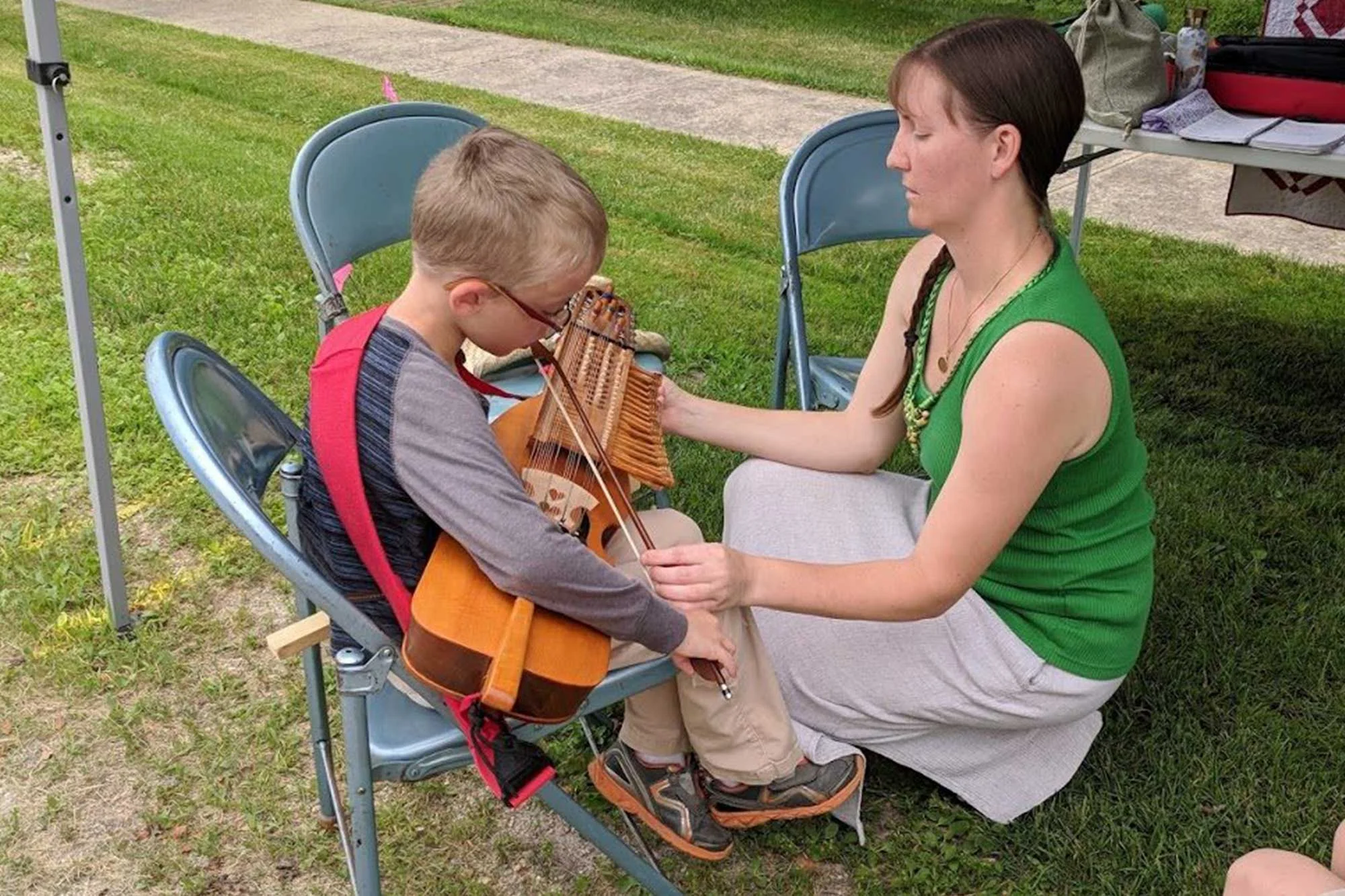 Janette Dragsvold helps a young child play the Nyckelharpa