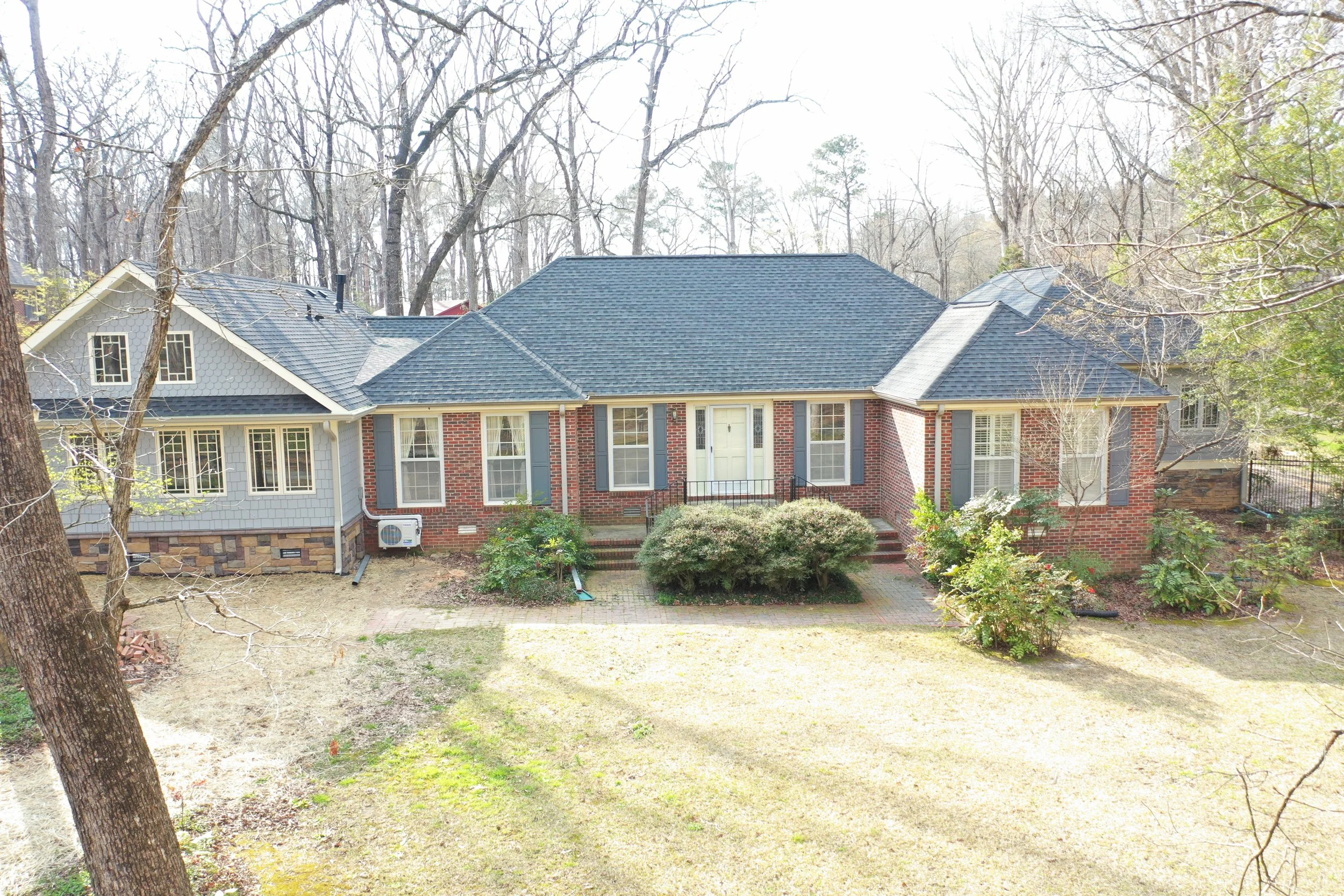 Front view of a brick house with a blue roof, surrounded by trees and shrubs in the yard.