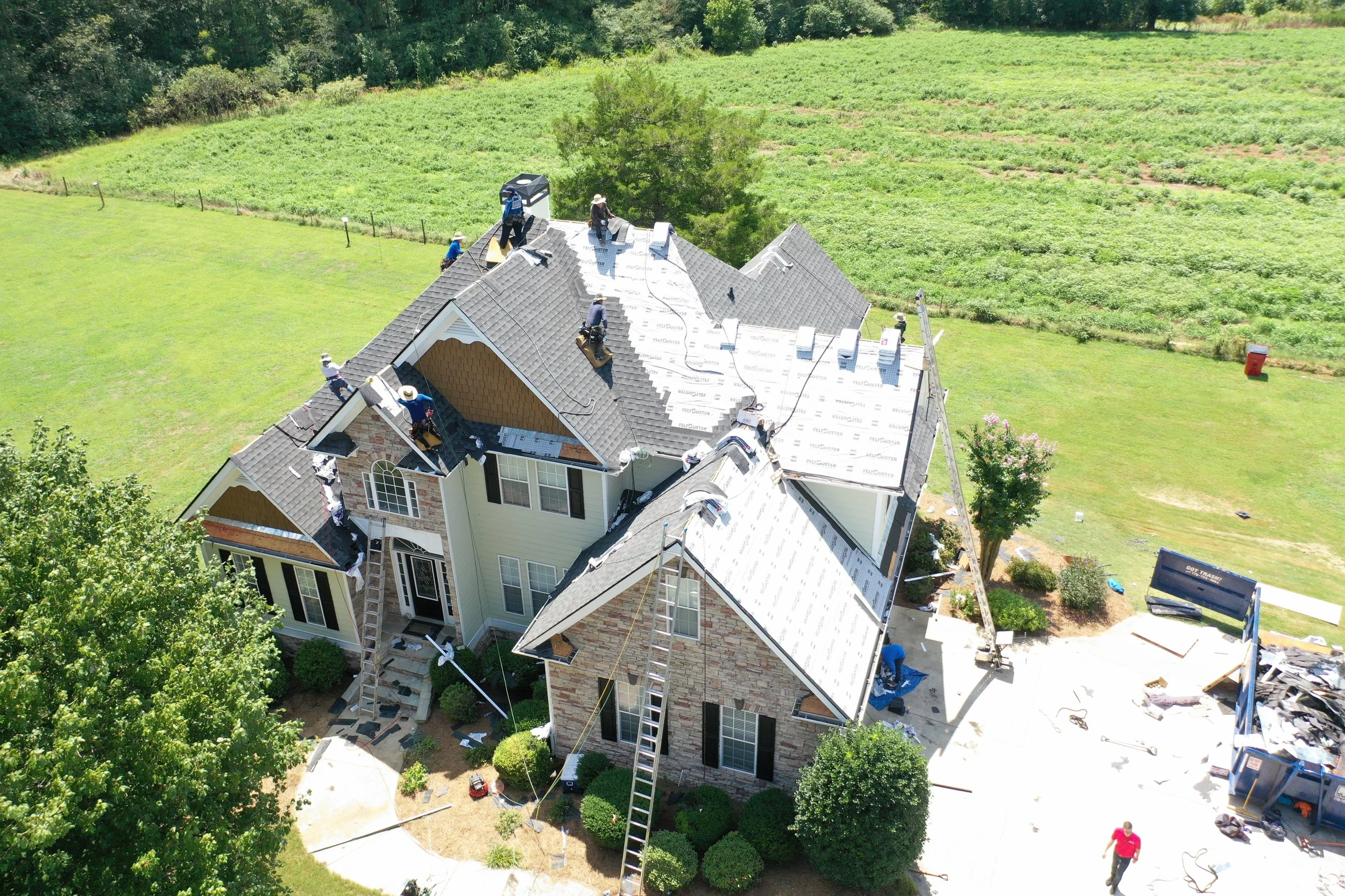 Aerial view of a large house with construction workers working on the roof, installing new shingles on the roof.
