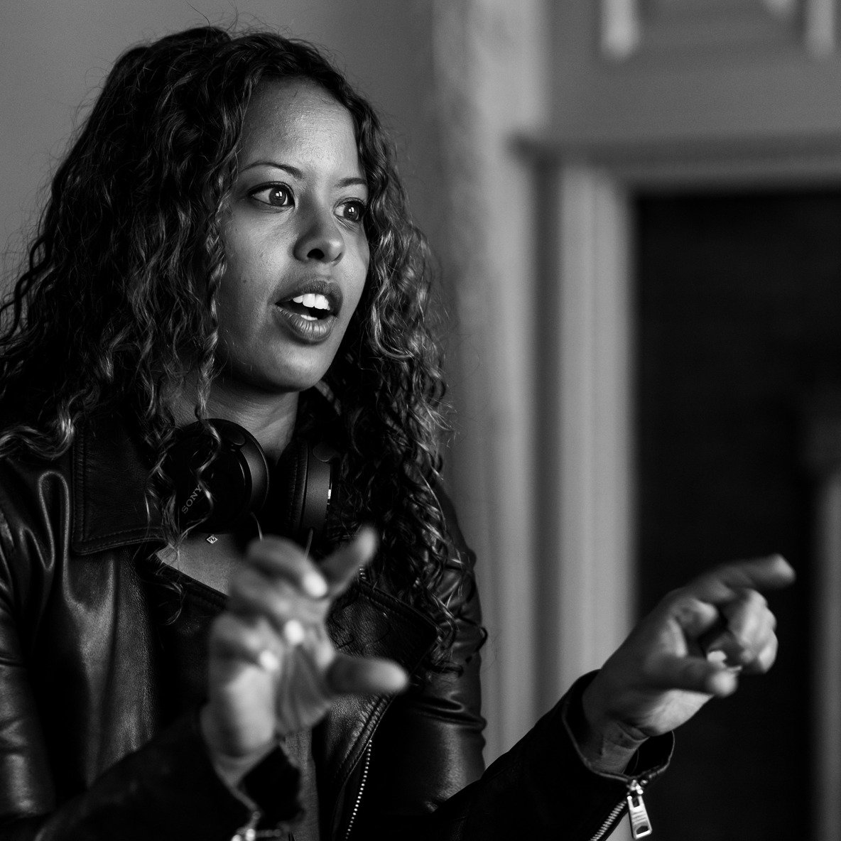 Idil Ibrahim mid-sentence while directing, gesturing with both hands, headphones around her neck