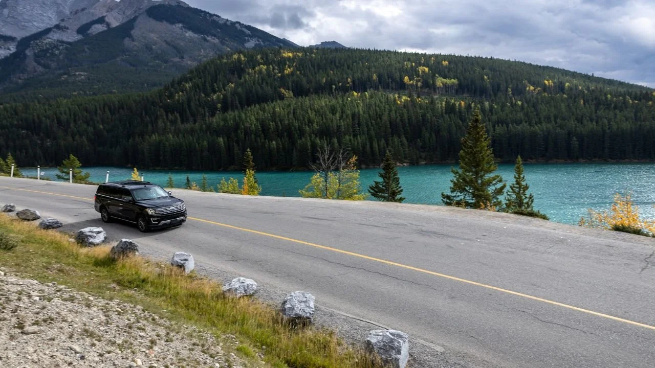SUV driving beside turquoise lake at Johnston Canyon.