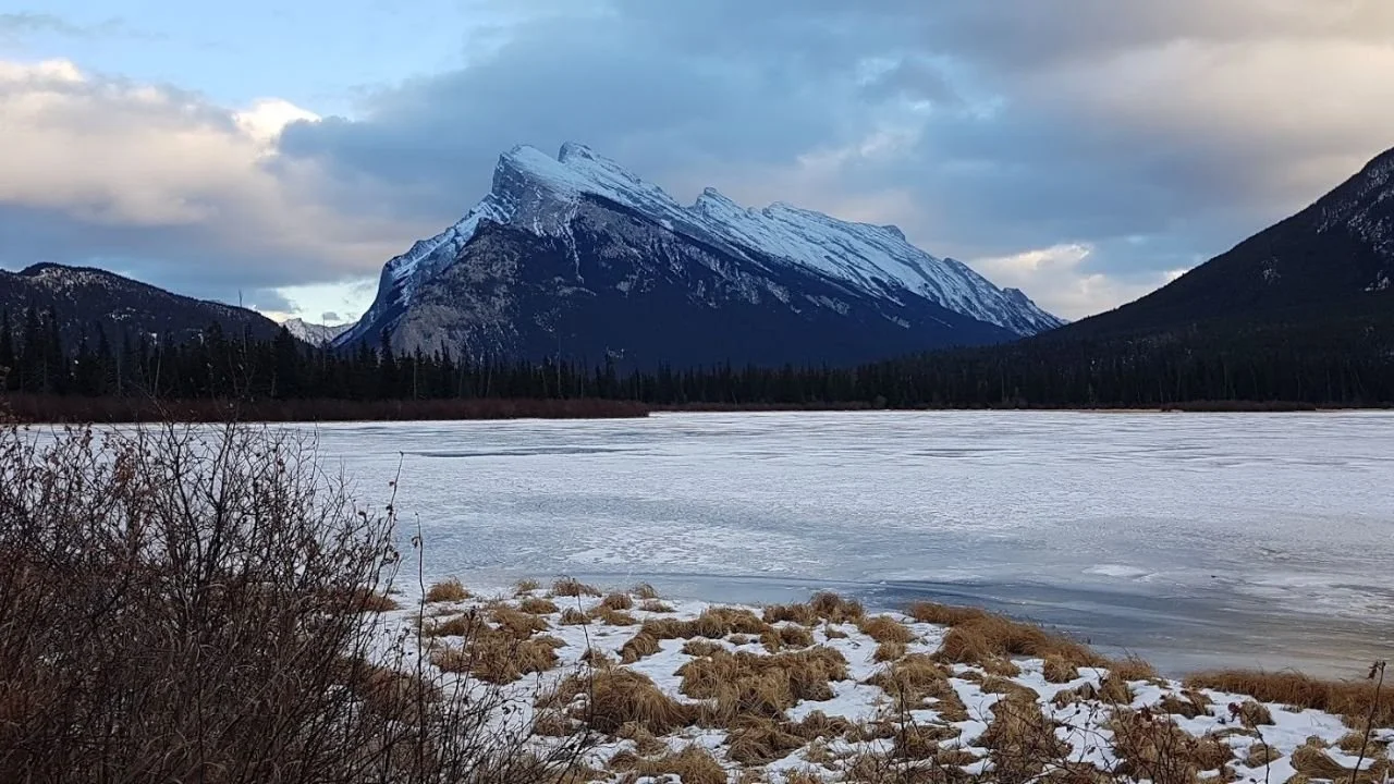 Frozen Vermilion Lakes in winter with snow-covered Mount Rundle rising beneath a cloudy sky near Banff.
