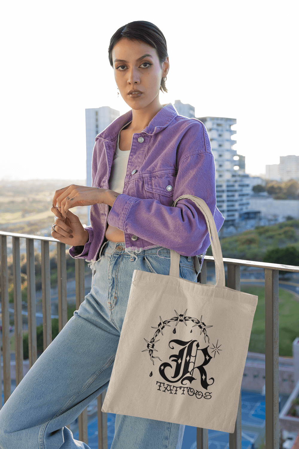 Model on a balcony in purple pants holding the john reardon tote.
