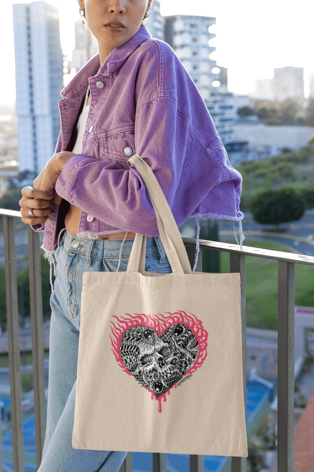 Mondel in a purple denim jacket standing on a balcony, holding the heart skull tote.
