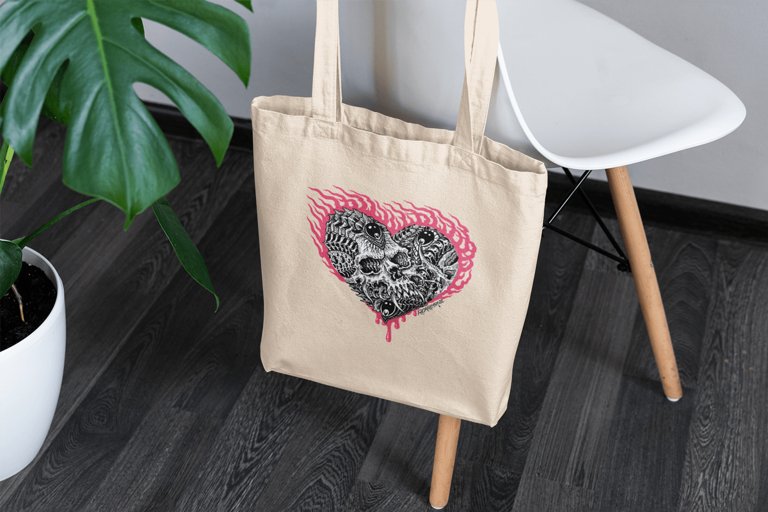 Organic cotton tote with tattoo graphic design hanging on a chair next to a lucious green plant and white table.