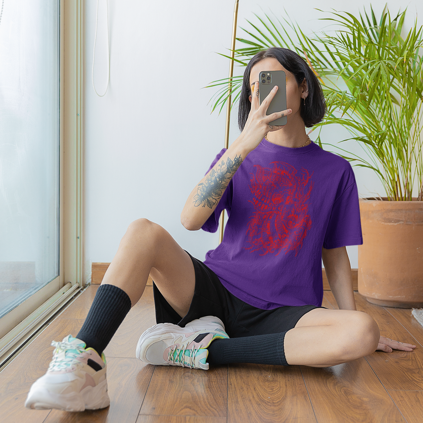Model taking a selfie at home by window wearing a purple John Reardon t-shirt with red print