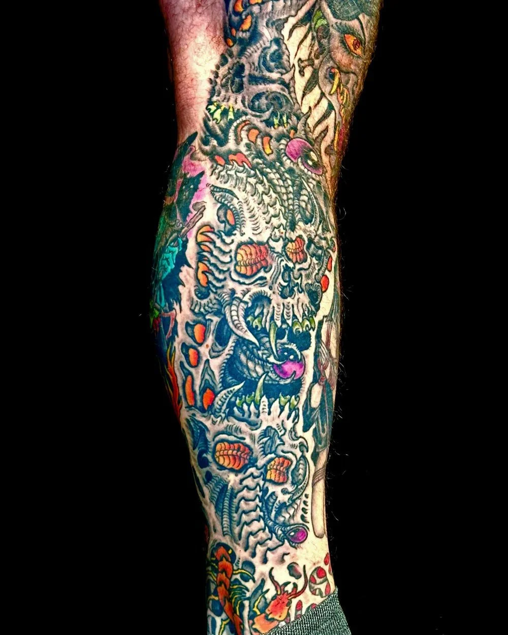 Drawn-on biomech color tattoo of stacked skulls in a skin rip by NYC tattoo artist.