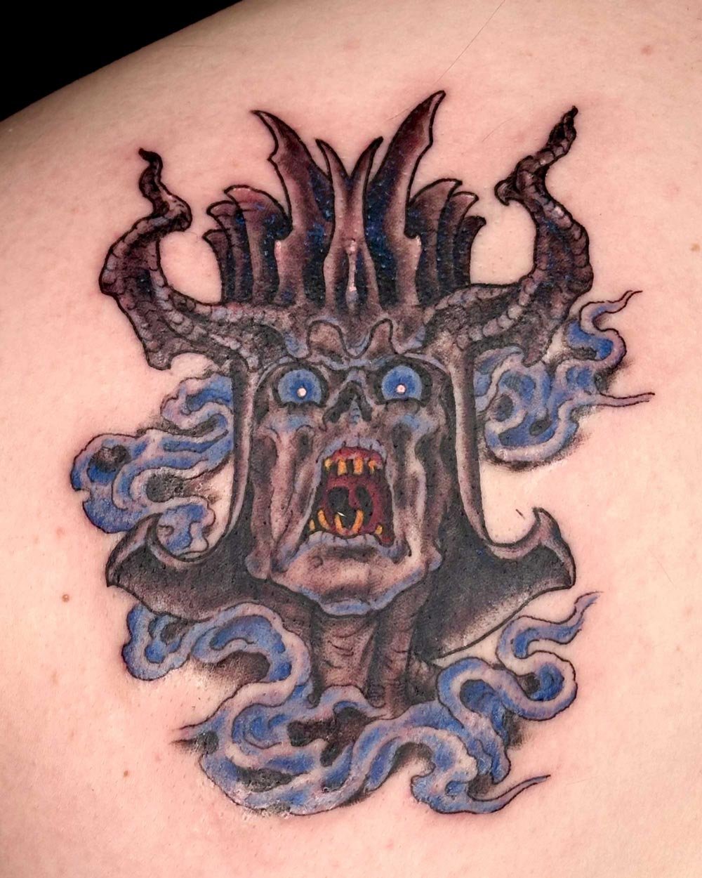 Color tattoo of a tree monster with blue smoke on the back of a shoulder.