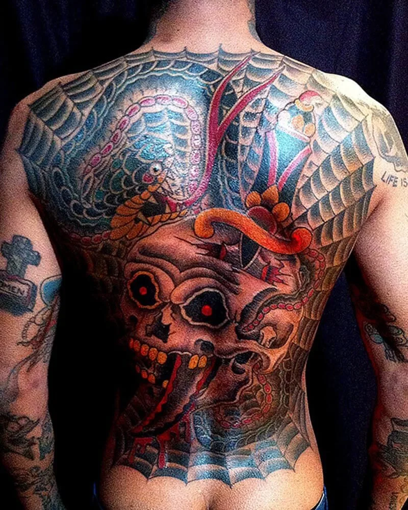 Full backpiece tattoo in color of a skull with snakes and background spider web.