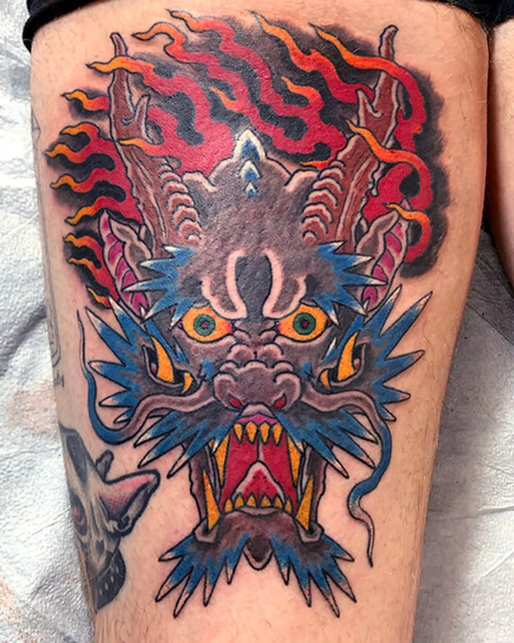 Large color red and blue tattoo of a Japenese dragon on a thigh.