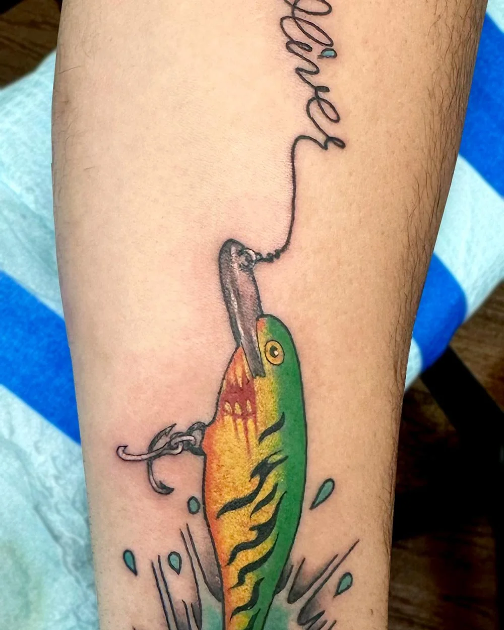 Upstate NY tattoo in color of a fish lure qith fish line in a name.