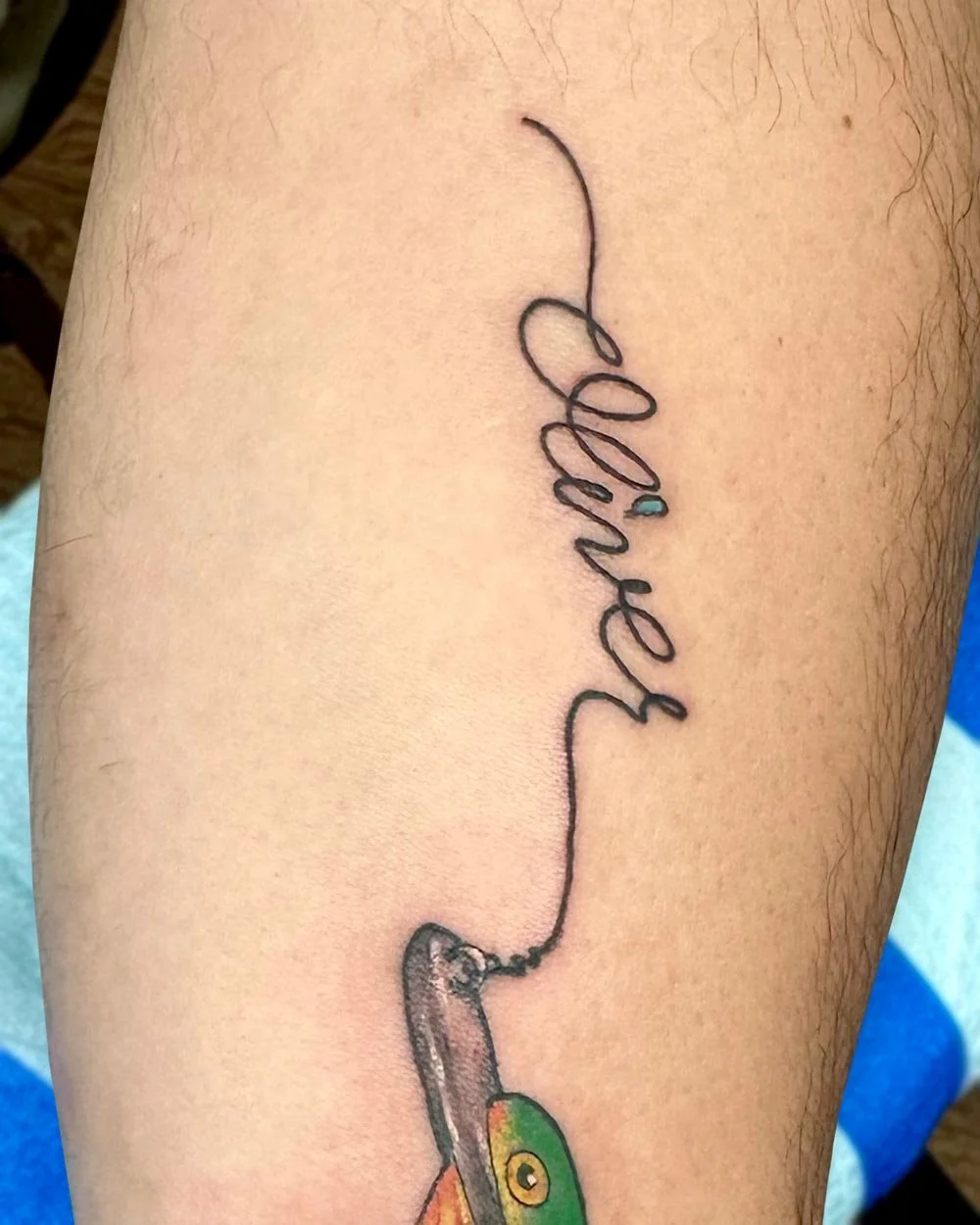 Cursive hand-written script tattoo with a fish lure in a color illustrative style.