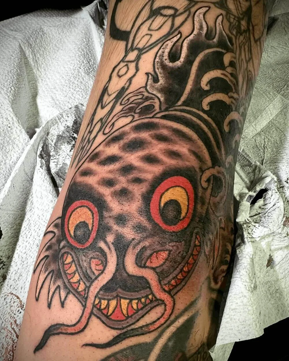 Japanese color fish tattoo on an arm with waves in the background.