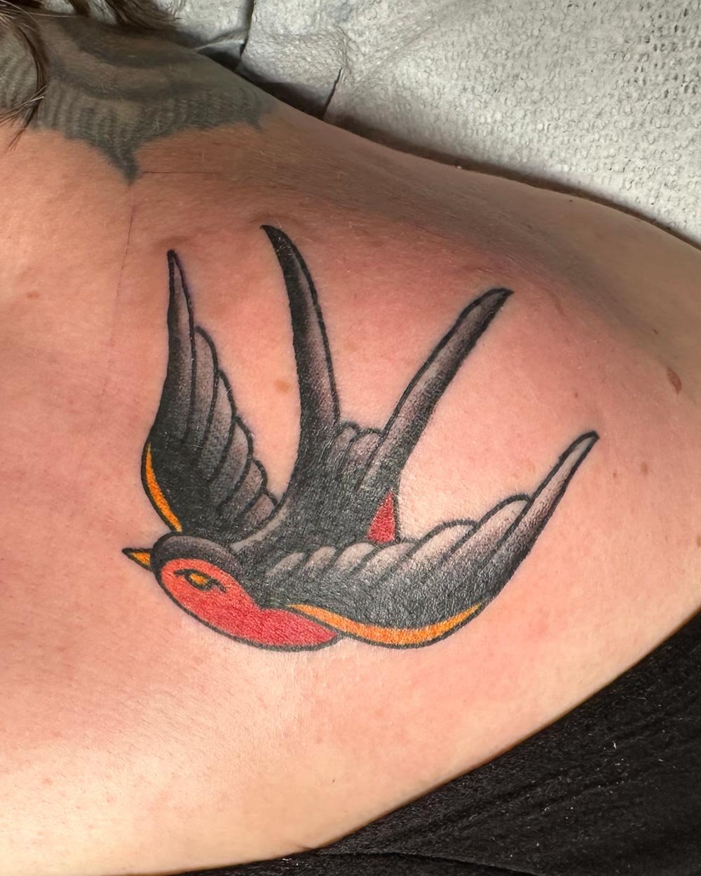 Traditional tattoo of a red and yellow sparrow on collarbone.