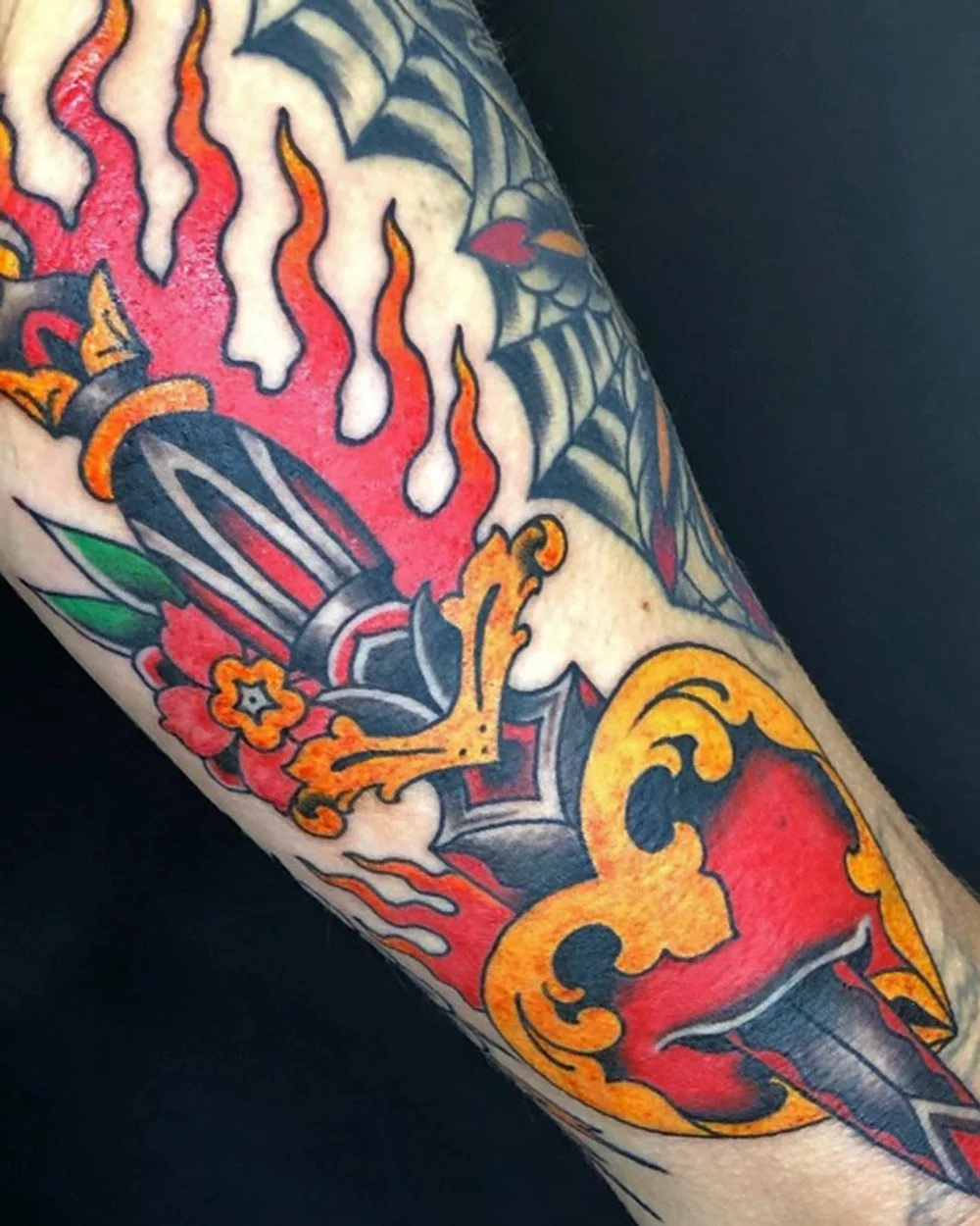 Traditional color tattoo of a dagger and heart on fire.