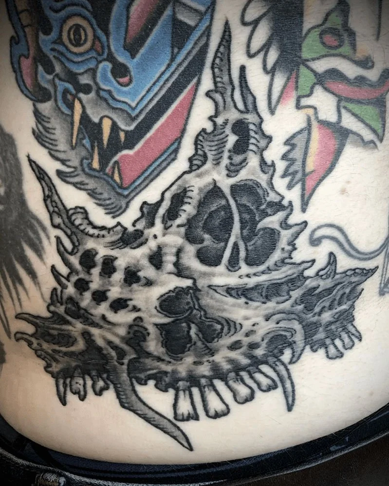 Drawn-on filler tattoo in black and grey of a biomechanical skull.