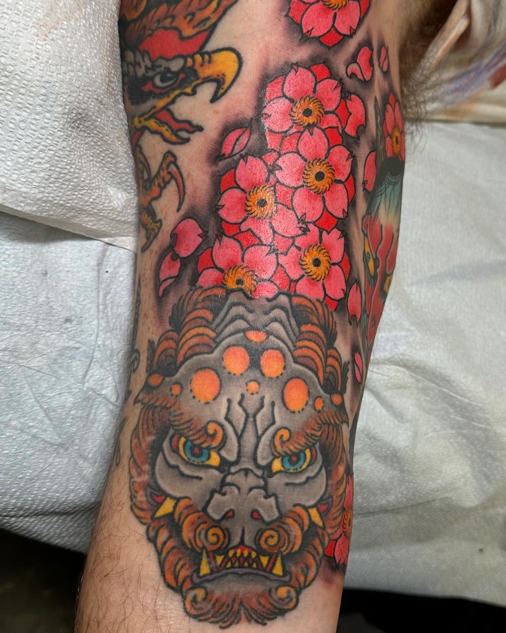 Color tattoo on an upper arm of a Foo dog with cherry blossoms.
