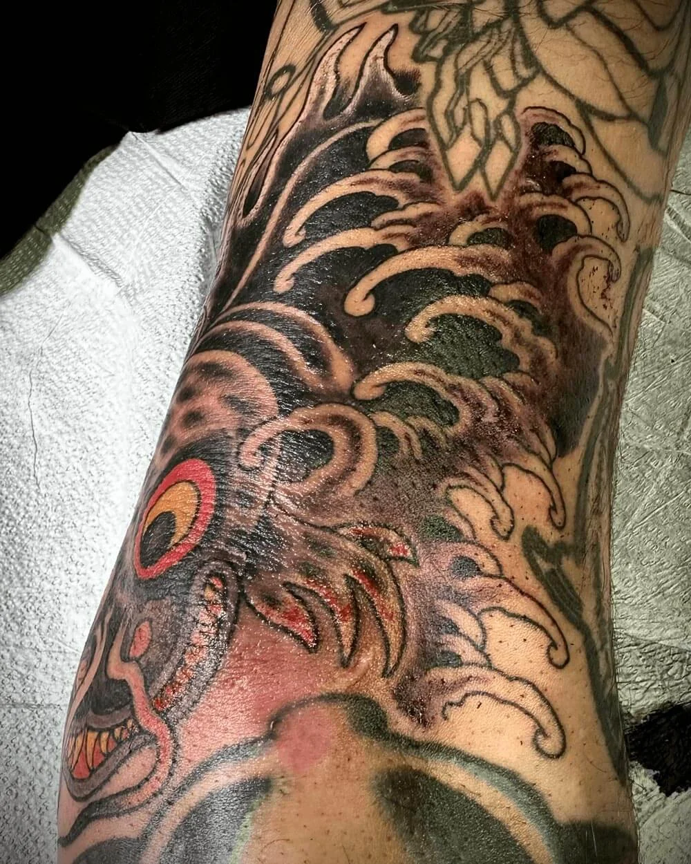 Color tattoo by John Reardon of a Japanese fish with waves in the back.