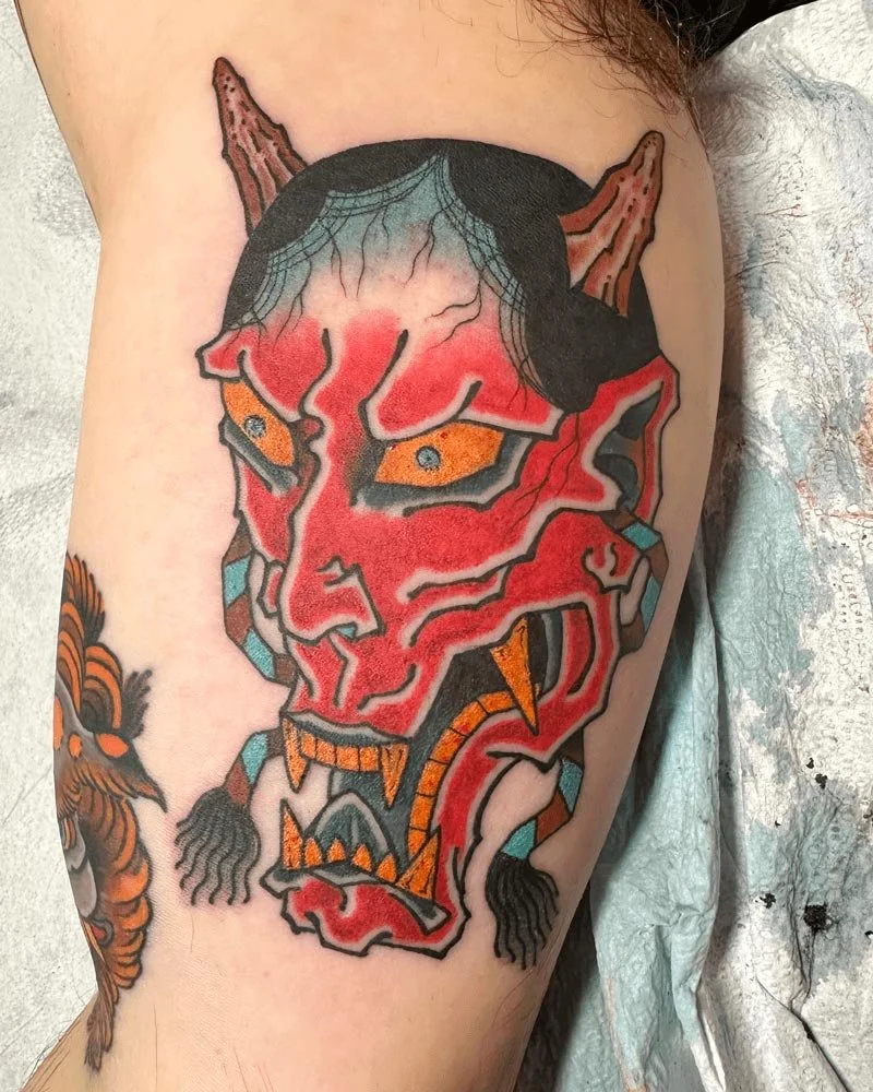 Red Hanya mask tattoo in color on inner arm by John Reardon.