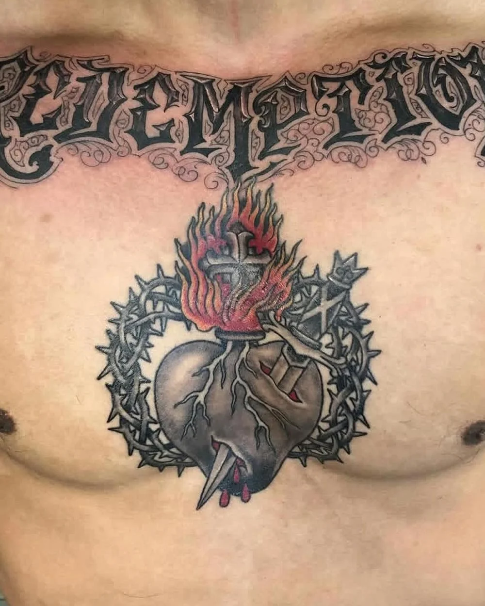 Chest sternum color tattoo of a flaming sacred heart with a sword through it.