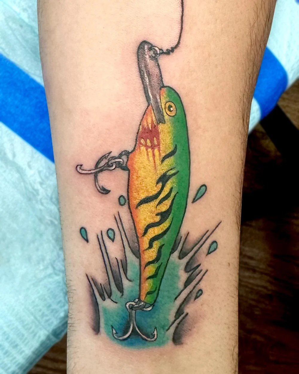 Fine line fishing tattoo in color of a green and yellow fish lure with name.