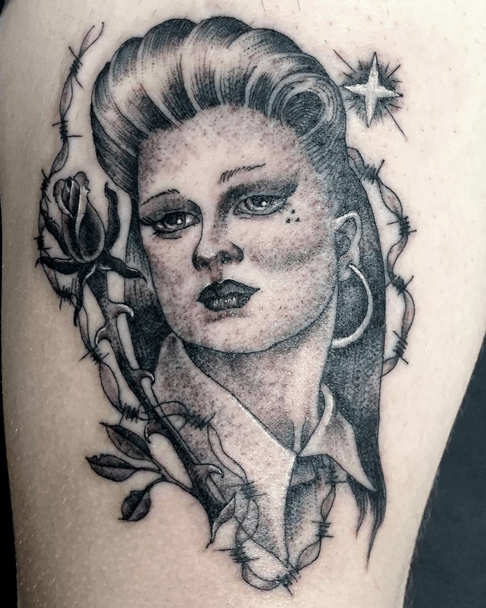 Leg tattoo in black and grey of a fineline portrait tattoo of a woman with barbed wire and roses.