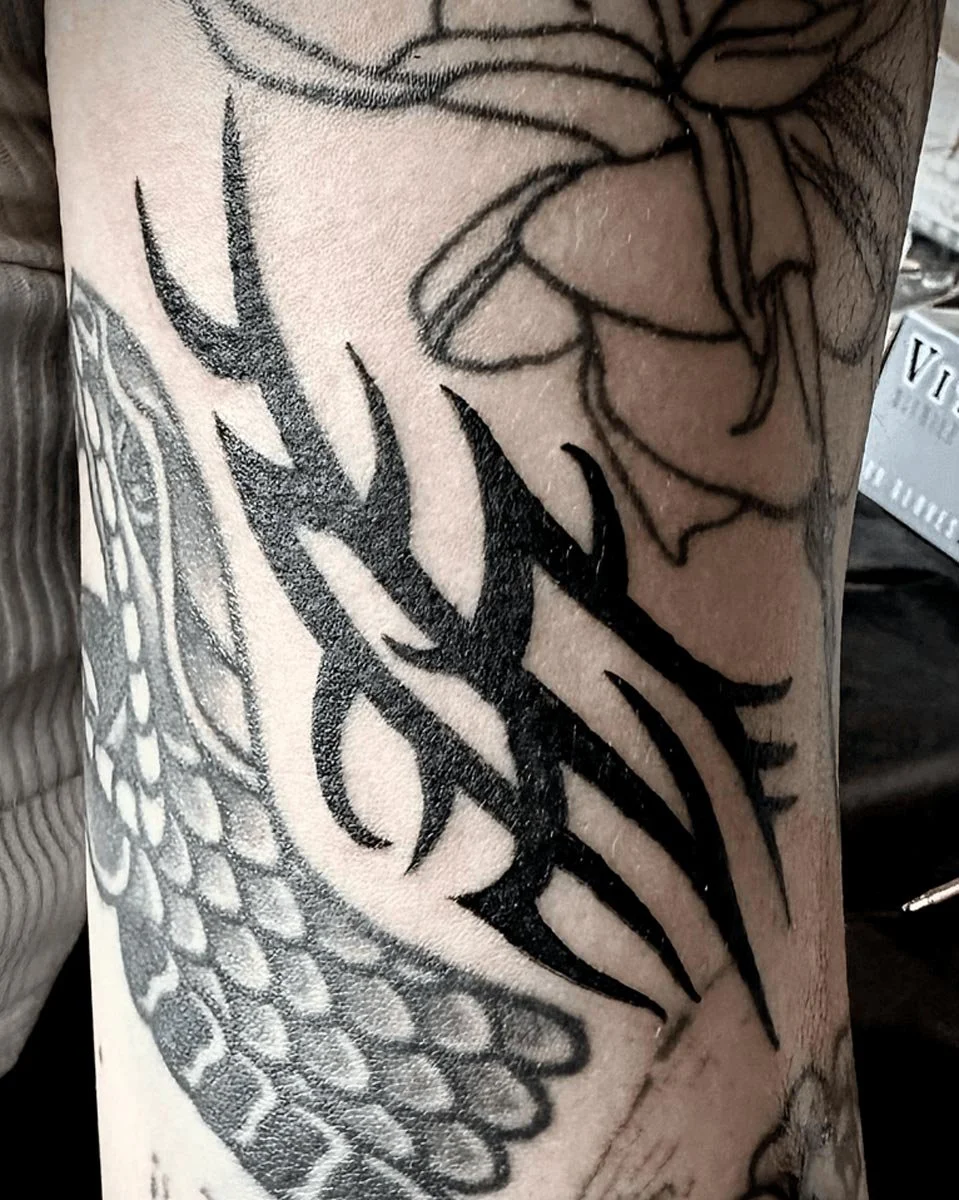 Tribal filler tattoo drawn-on and tattooed in black and grey between other tattoos.