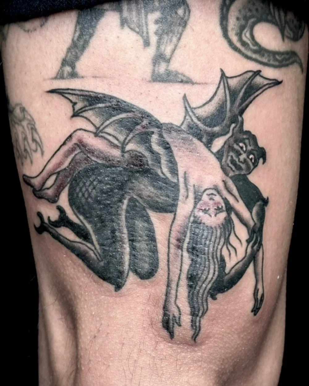 Black and grey tattoo of a person being scooped up and flown away by a devil.