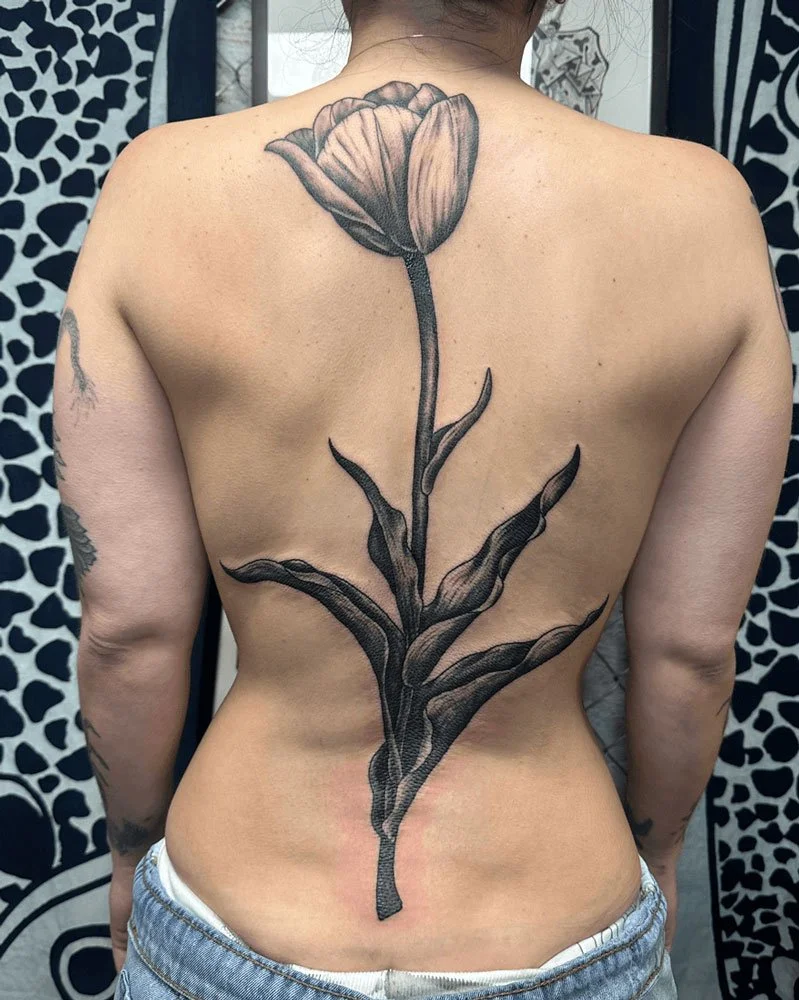 Beautiful realistic tulip tattoo in black and grey along the spine.