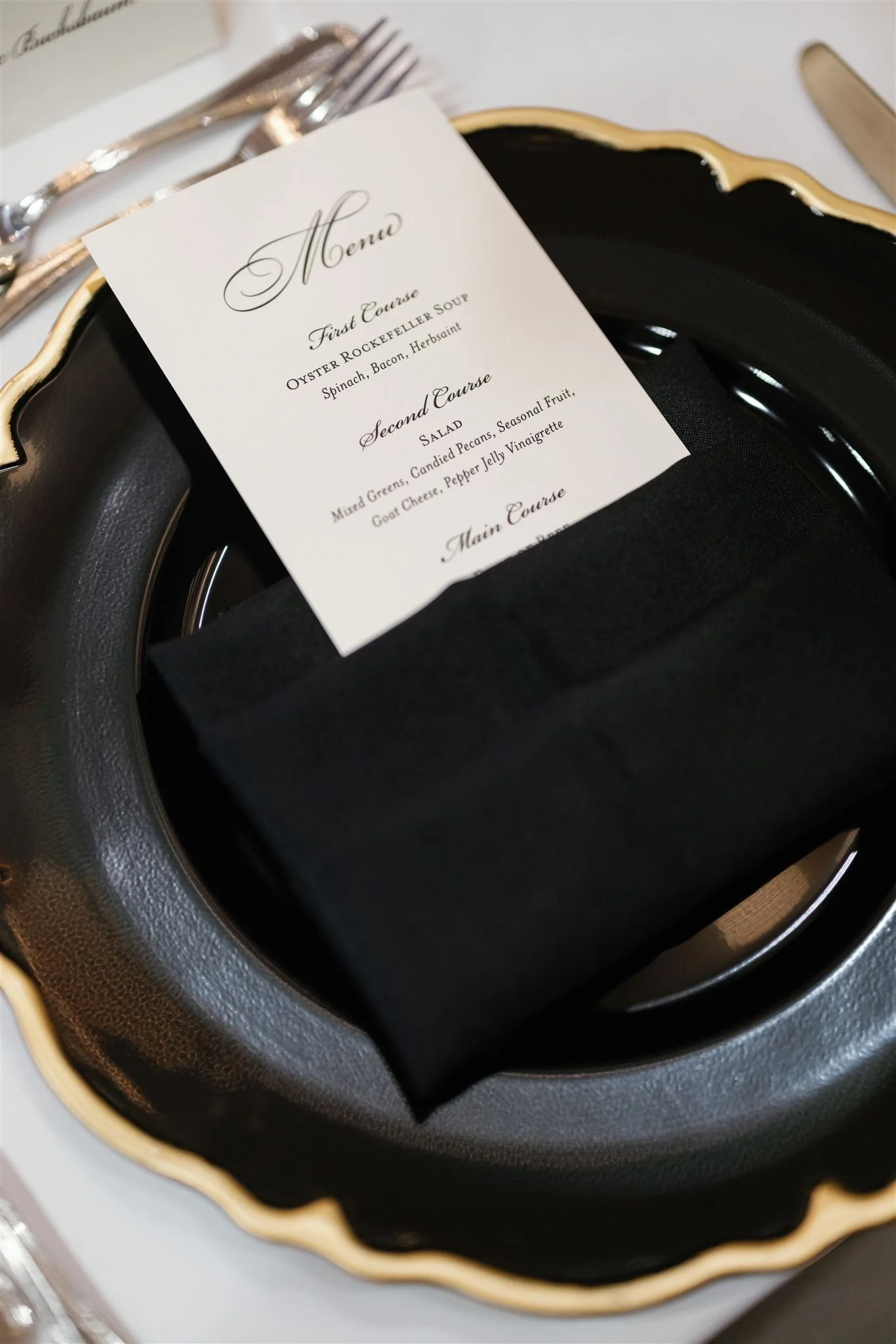 A black and gold decorative tray holding a menu with elegant cursive writing, silverware, and a white tablecloth.
