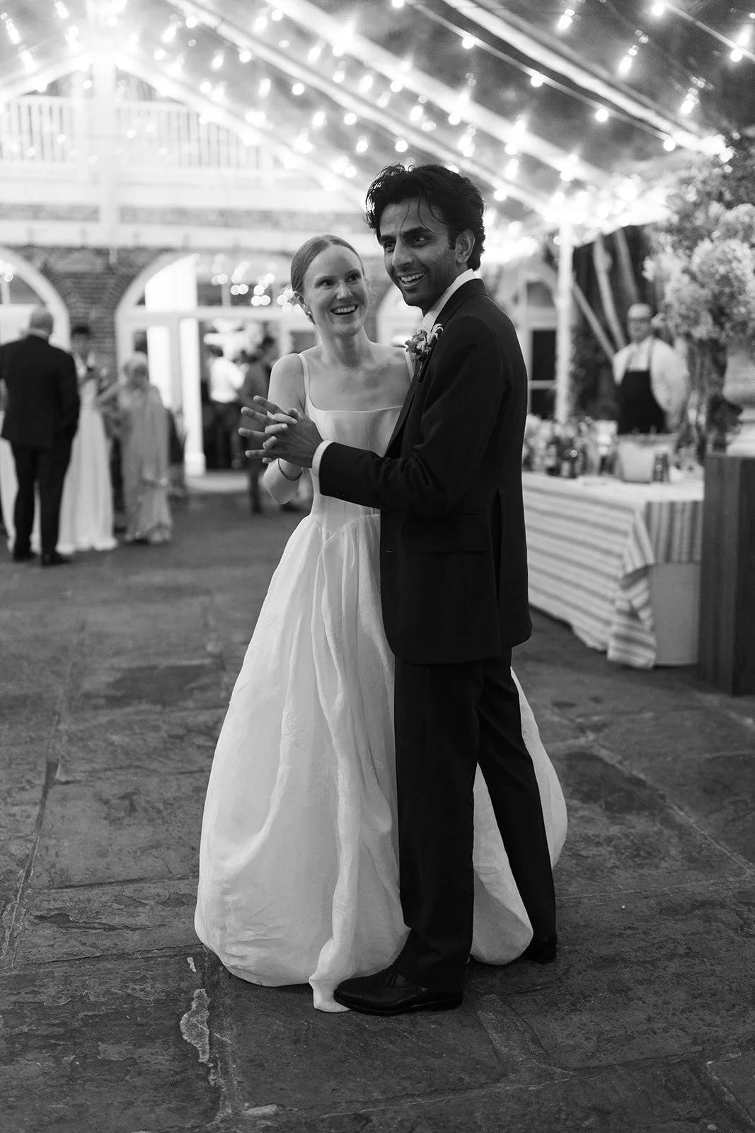 A bride and groom happily dance at their wedding reception in Brennan's New Orleans courtyard with string lights, friends, and family in the background.