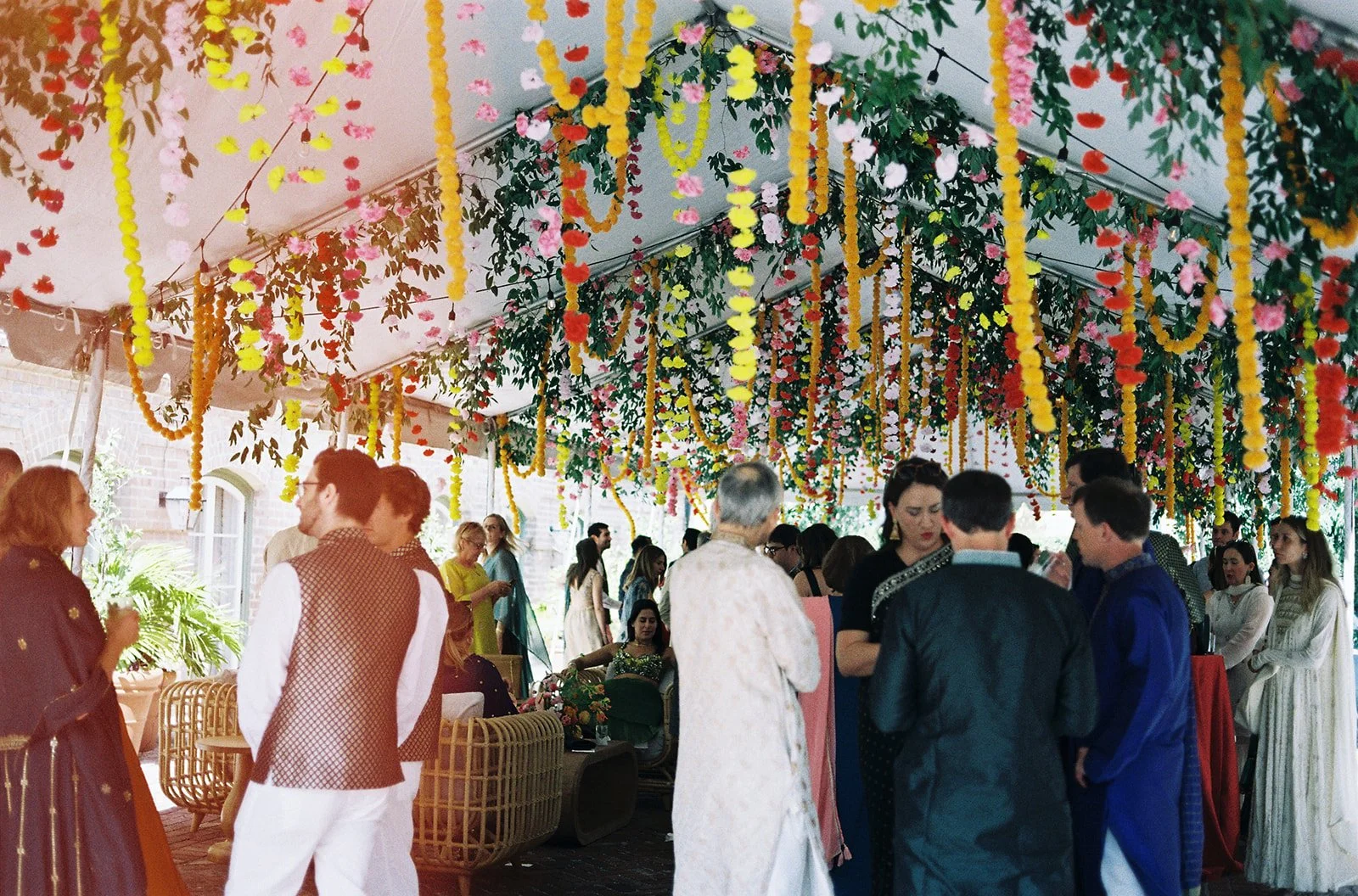 People attending a lively celebration under a decorated canopy with pink, yellow, red, and white floral arrangements and hanging garlands. Hotel Peter and Paul wedding by Everly Event Planning & Design.