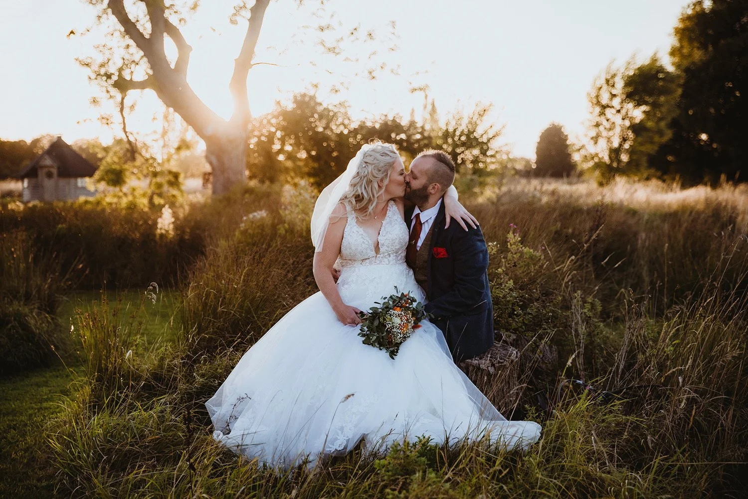 Bride and groom sitting on log at sunset at Thetford Farm Barn
