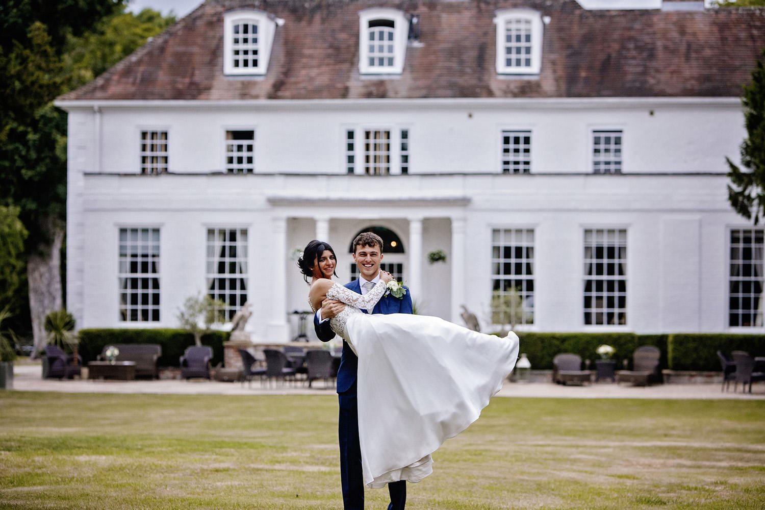 Groom carrying bride in front of Barrington Hall