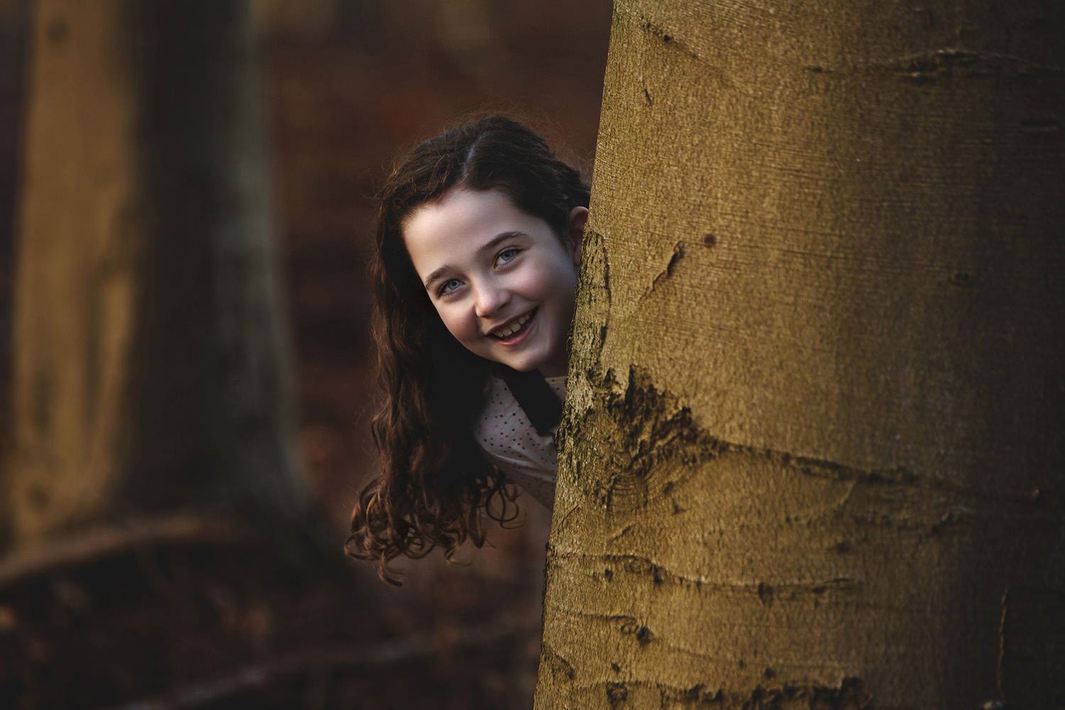 Girl peering from behind tree