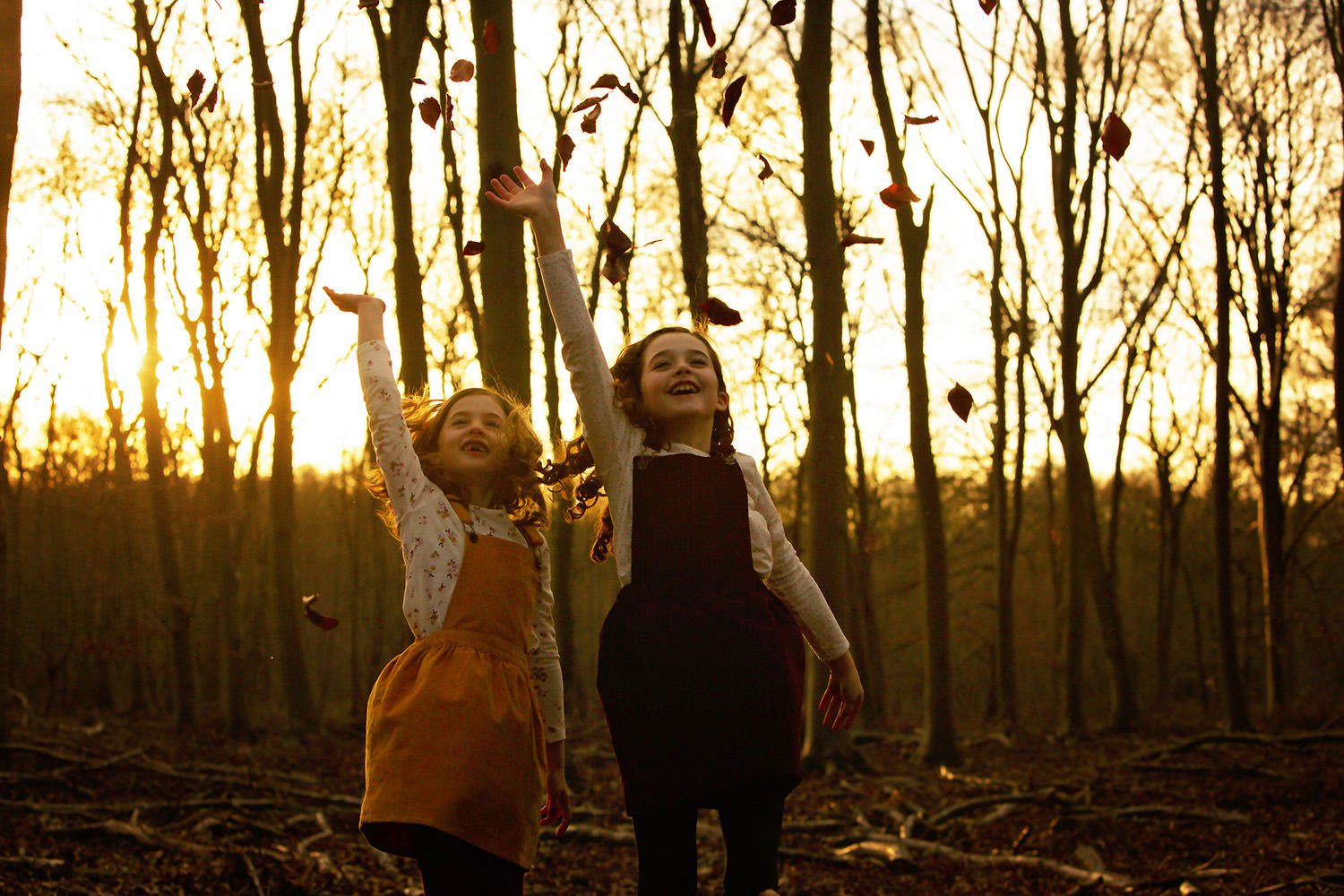 Sisters throwing leaves into winter sun