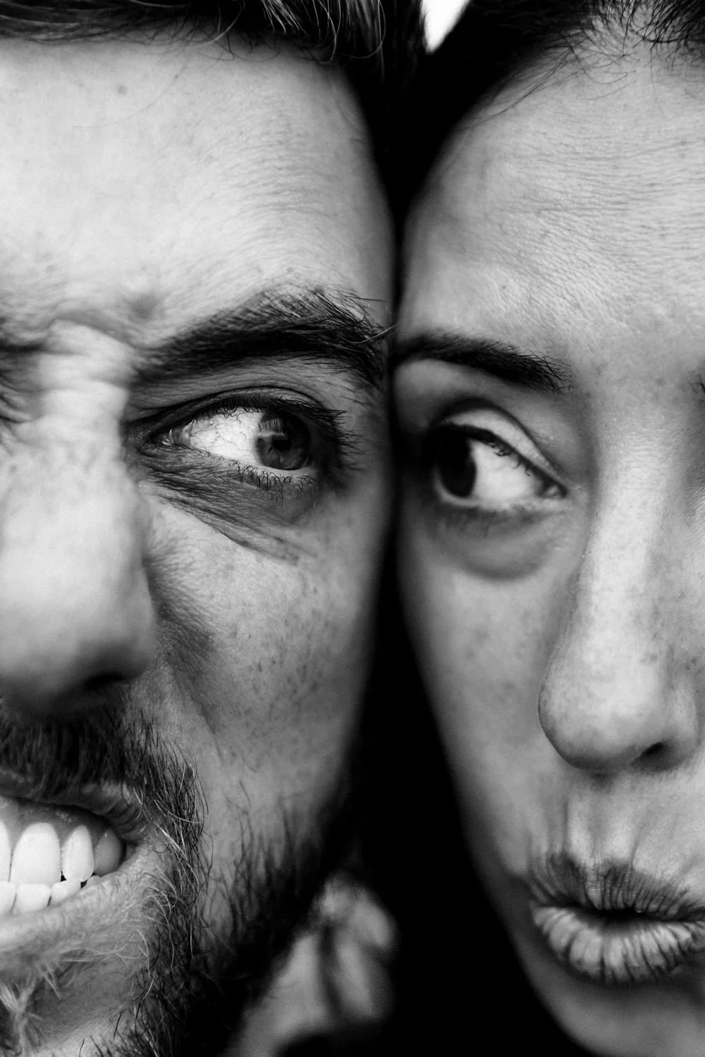 Close-up black and white photo of two people’s faces, showing their eyes and partial facial features pressed closely together.