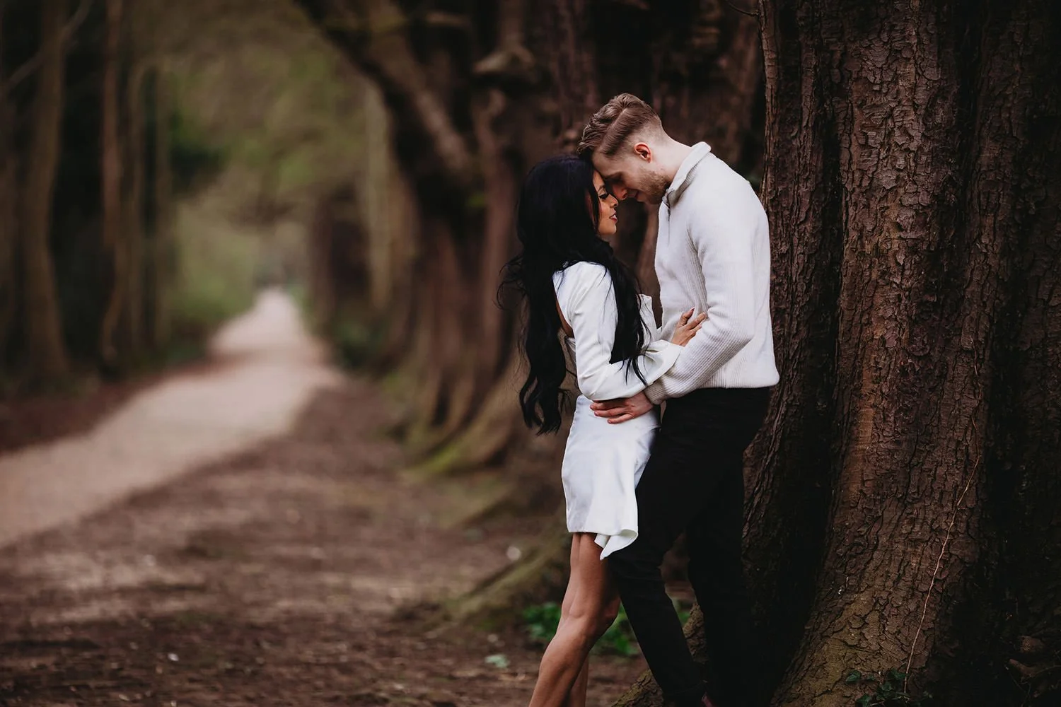 Engaged couple in Huntingdon leaning against a large tree at Hinchingbrooke Country Park