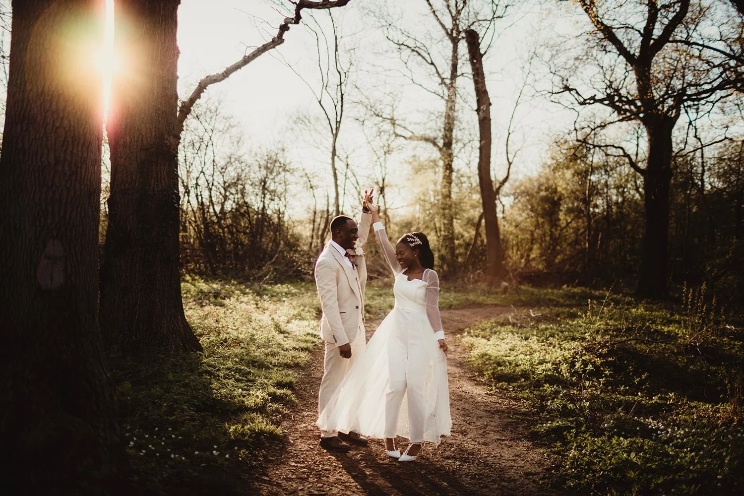 A newlywed couple dancing together on a forest path during sunset, surrounded by trees and greenery.