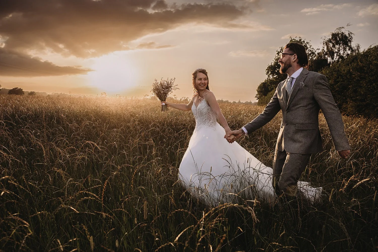 Bride running with groom through wheatfield at sunset