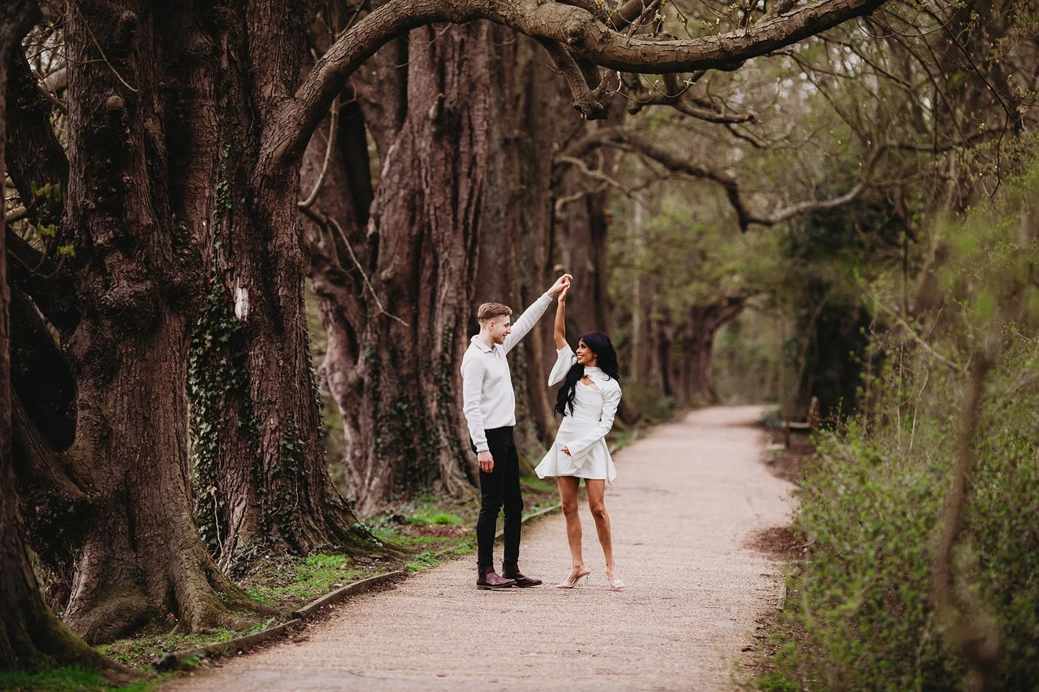 A couple dancing on a forest path surrounded by tall trees.