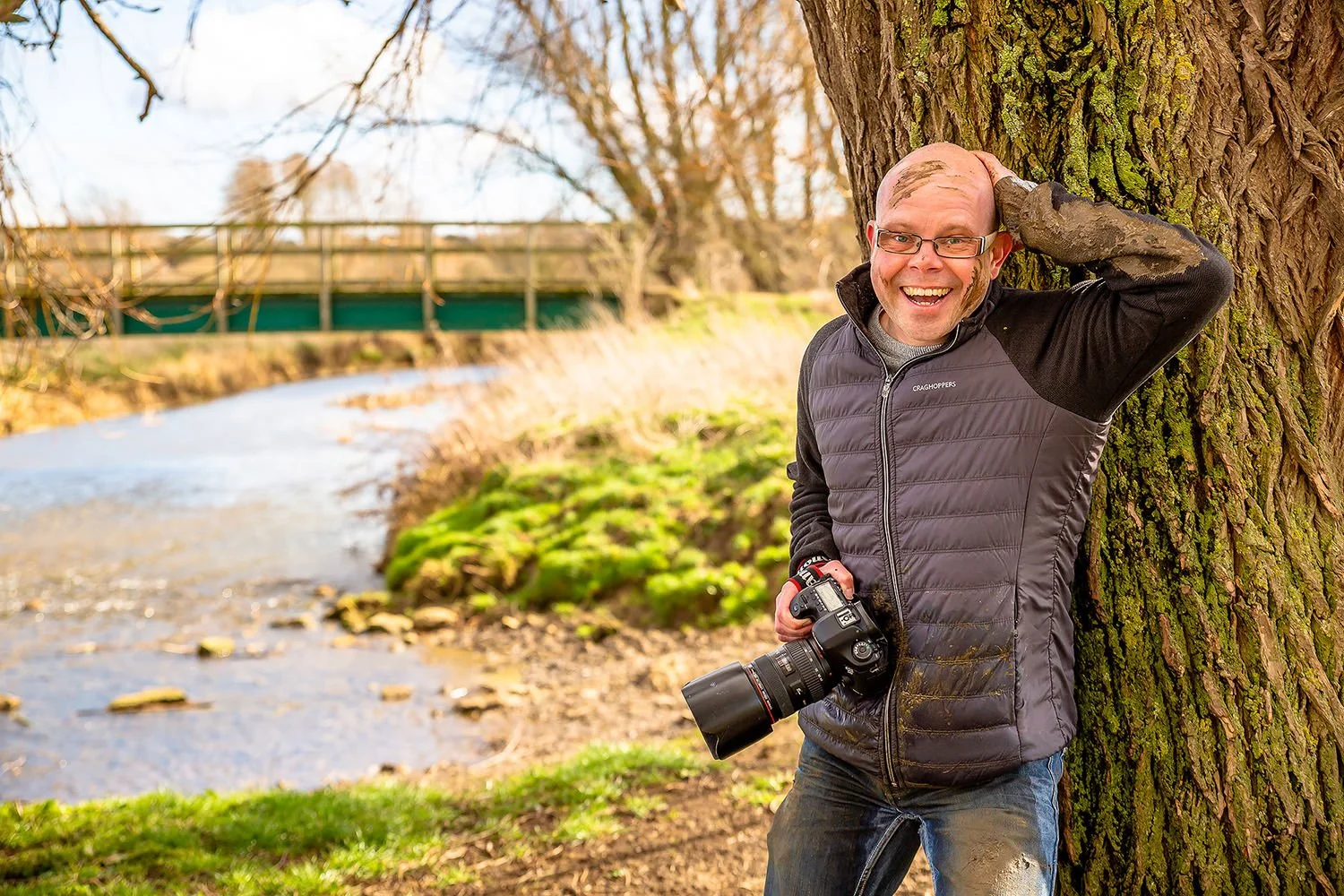 Man carrying a camera and smiling next to a river