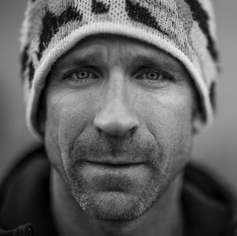 Close-up of a man with light facial hair wearing a winter hat, in black and white.