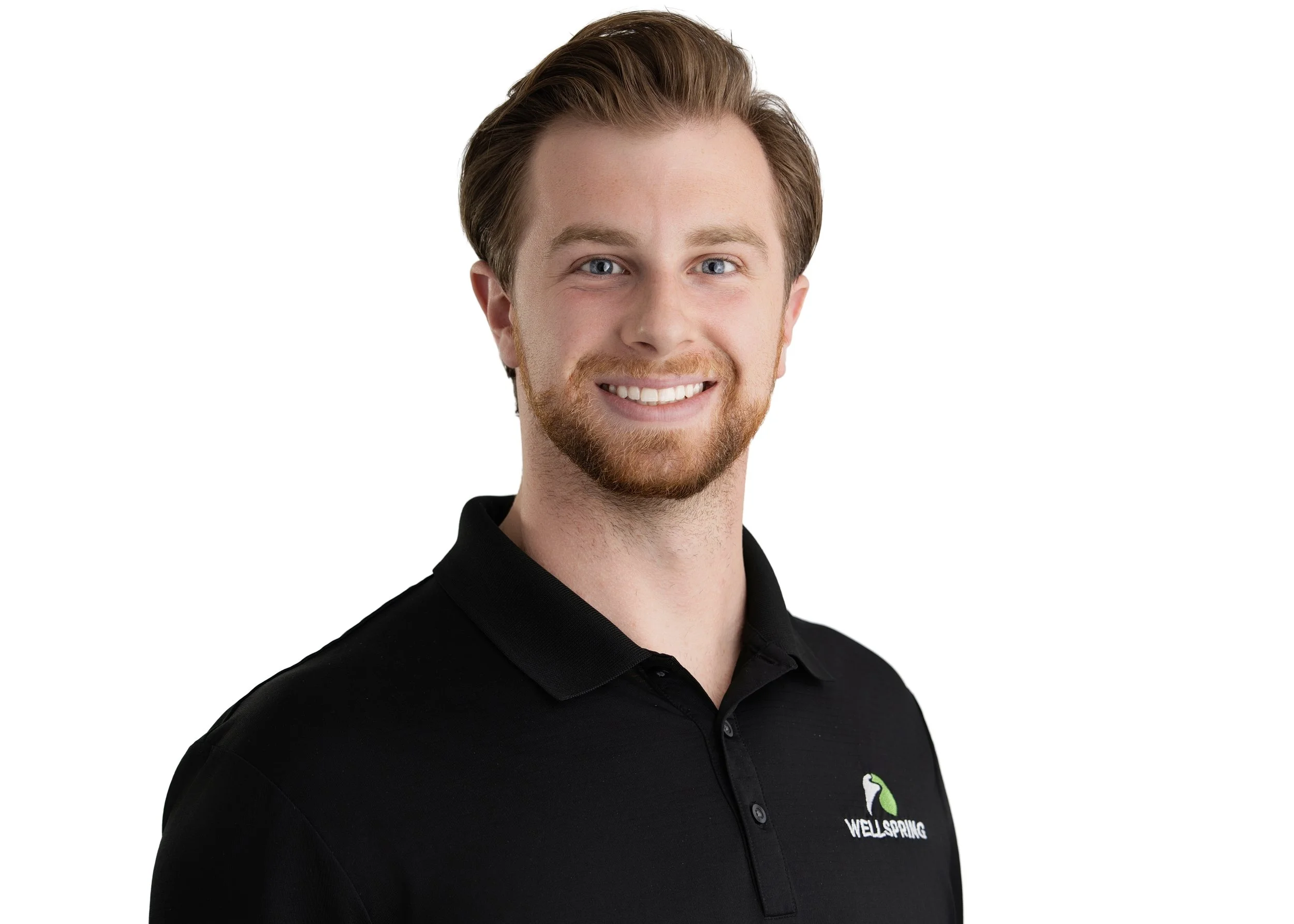 A young man with styled light brown hair and a beard, smiling, wearing a black polo shirt with a Wellspring logo, against a white background.