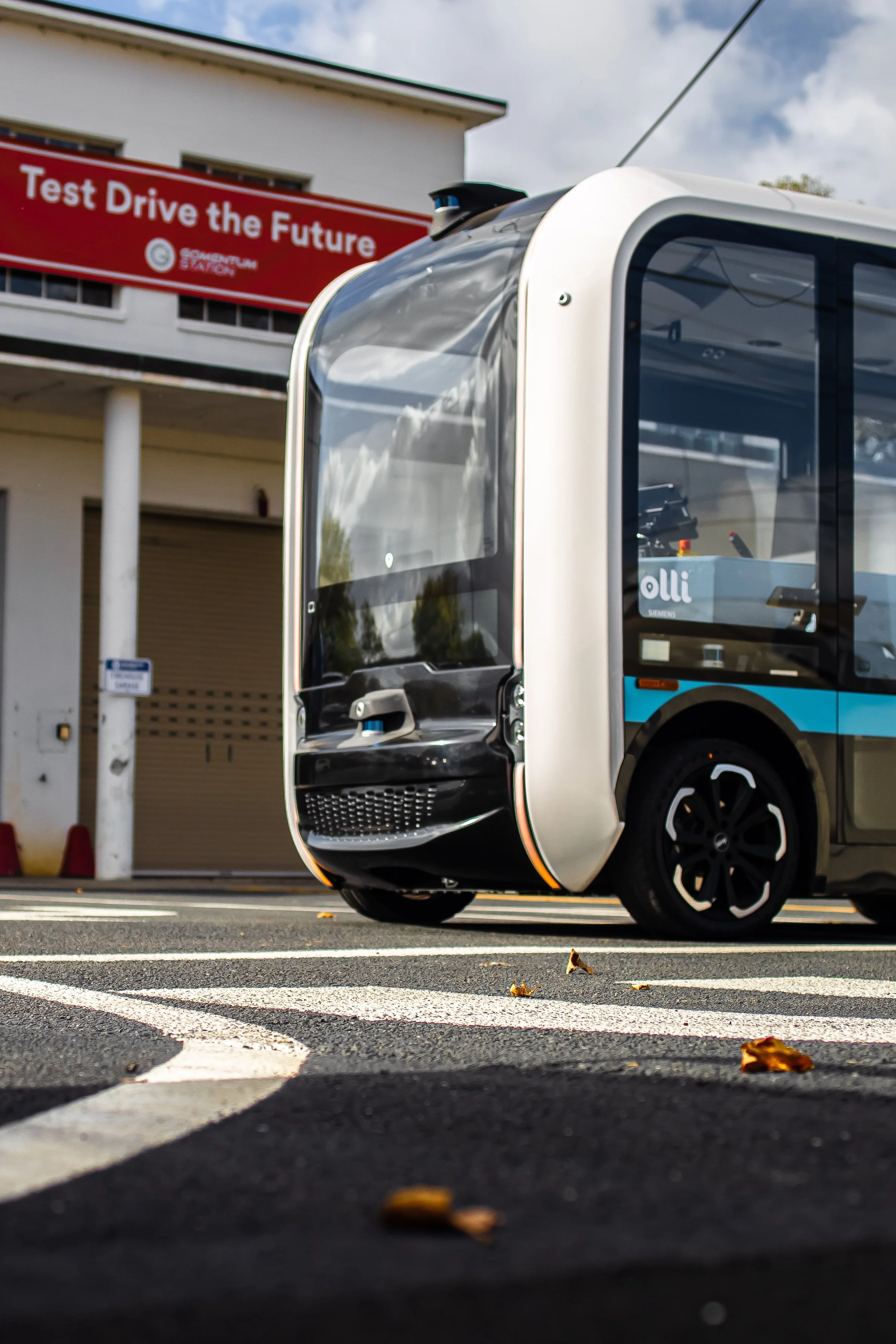 Autonomous electric shuttle bus parked in a designated area with a sign in the background that reads "Test Drive the Future."